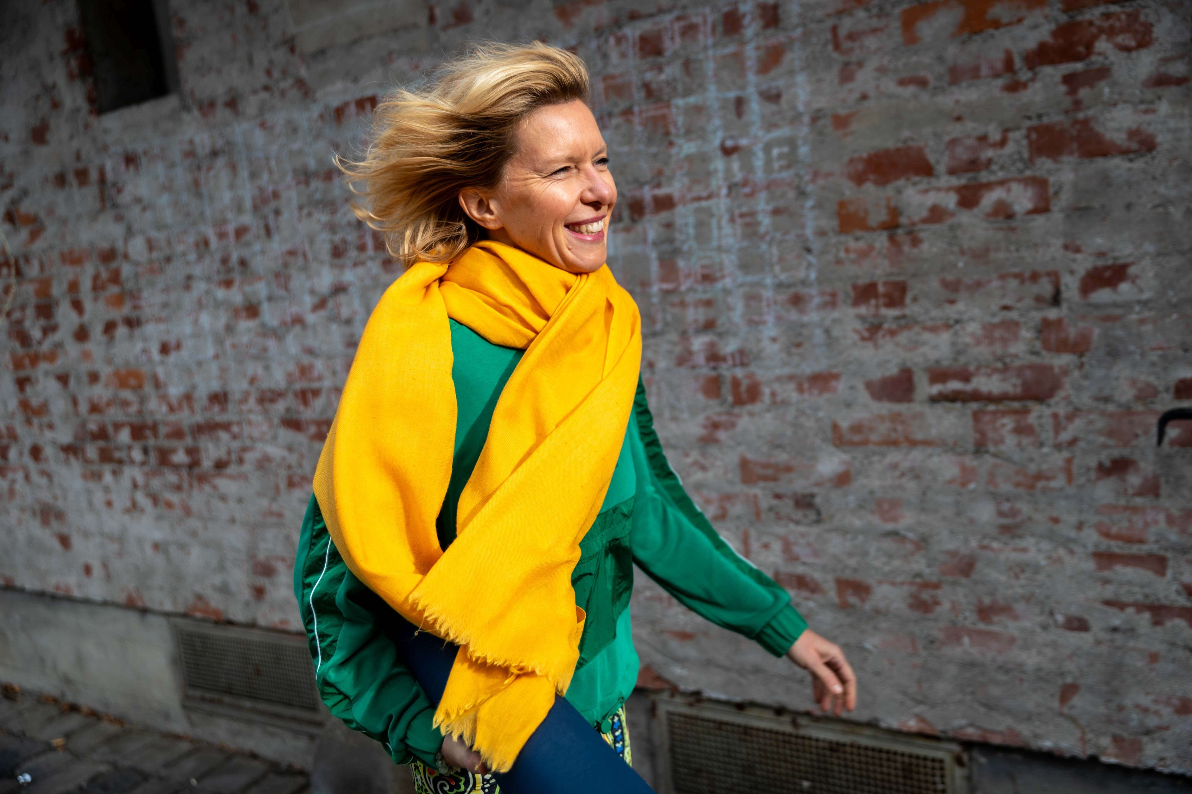 Karina Santjohanser, Gründerin von PRADIYA, lachend und schwungvoll mit gelbem Angora-Schal — Unternehmerin, Yogini, Sozialunternehmerin
